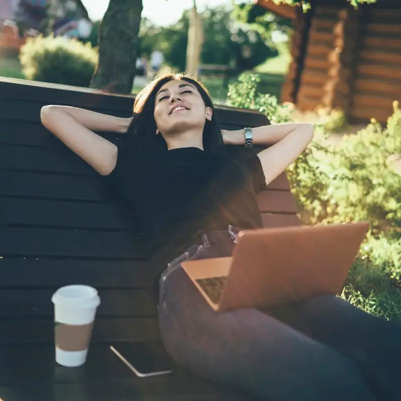 A woman leans back with closed eyes on an outdoor bench. She has finished working on her laptop and is enjoying her life after treatment at Sheridan Grove Recovery.