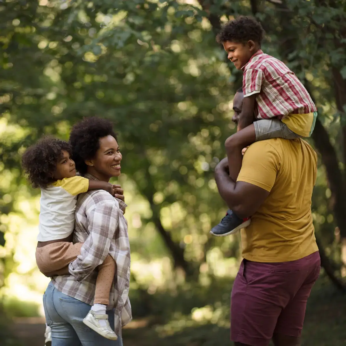 A husband and wife are giving their children piggy-back rides through a wooded area. They are feeling free and happy after co-occurring disorders treatment at Sheridan Grove Recovery.