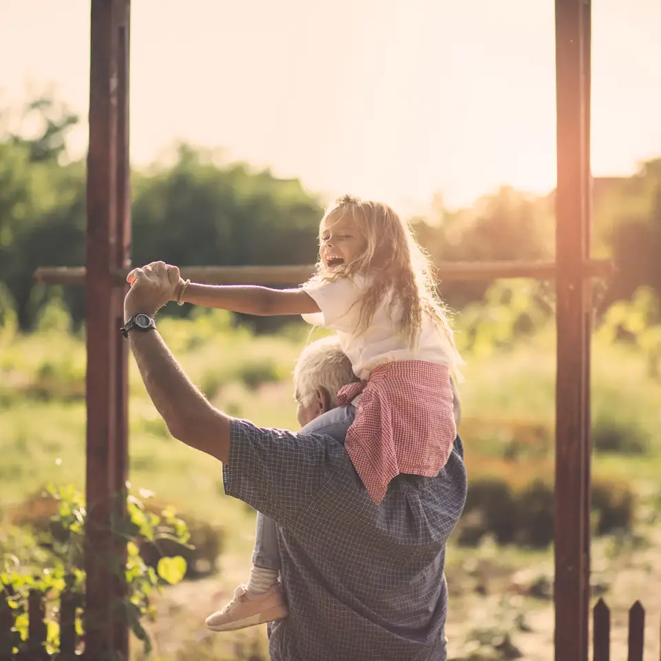 A little girl sits on top of her grandfather's shoulders as he walks through a garden. He's able to do things with his grandkids now that he's completed his residential treatment at Sheridan Grove Recovery.