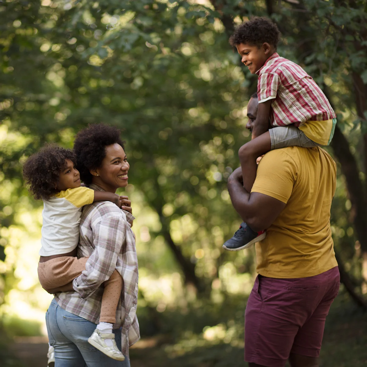 A husband and wife are giving their children piggy-back rides through a wooded area. They are feeling free and happy after co-occurring disorders treatment at Sheridan Grove Recovery.