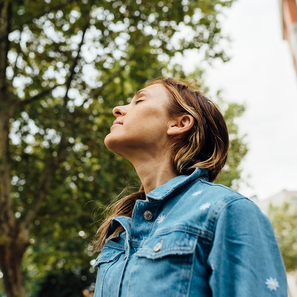 A woman stands peacefully outside with her eyes closed and head tilted toward the sky. This tranquility is what you can expect at Sheridan Grove Recovery.
