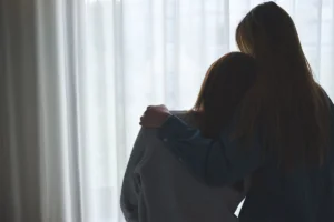 Silhouettes in front of window of a woman comforting her friend after relapse